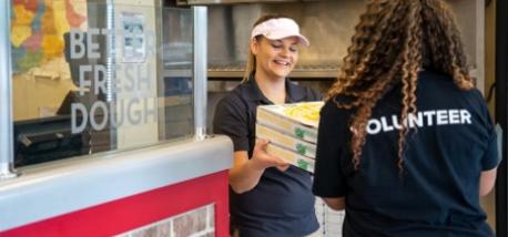 A Papa Johns team members hands surplus pizza orders to a volunteer.